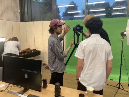 two teenagers and an adult facilitator working behind a camera and a green screen