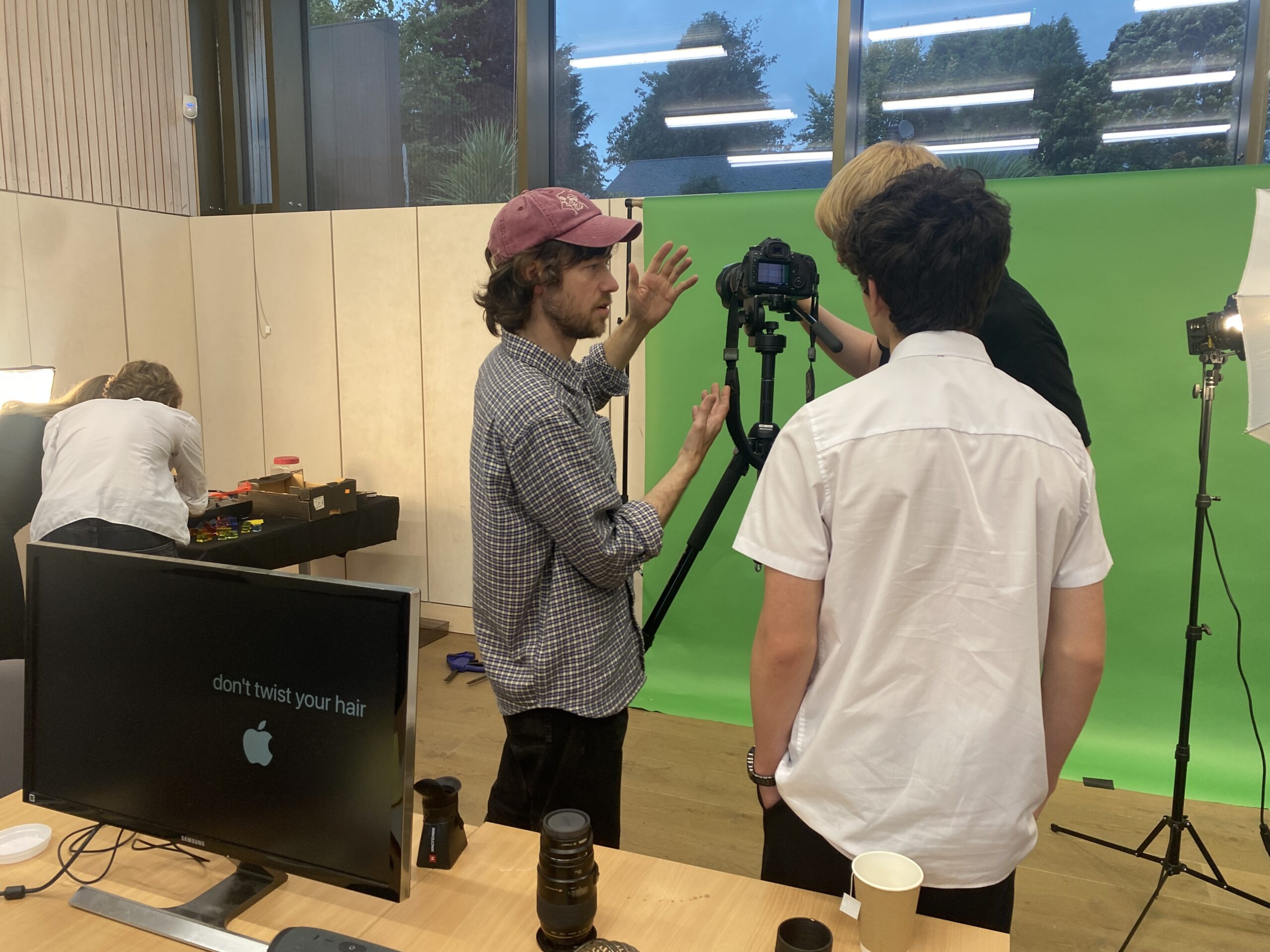 two teenagers and an adult facilitator working behind a camera and a green screen