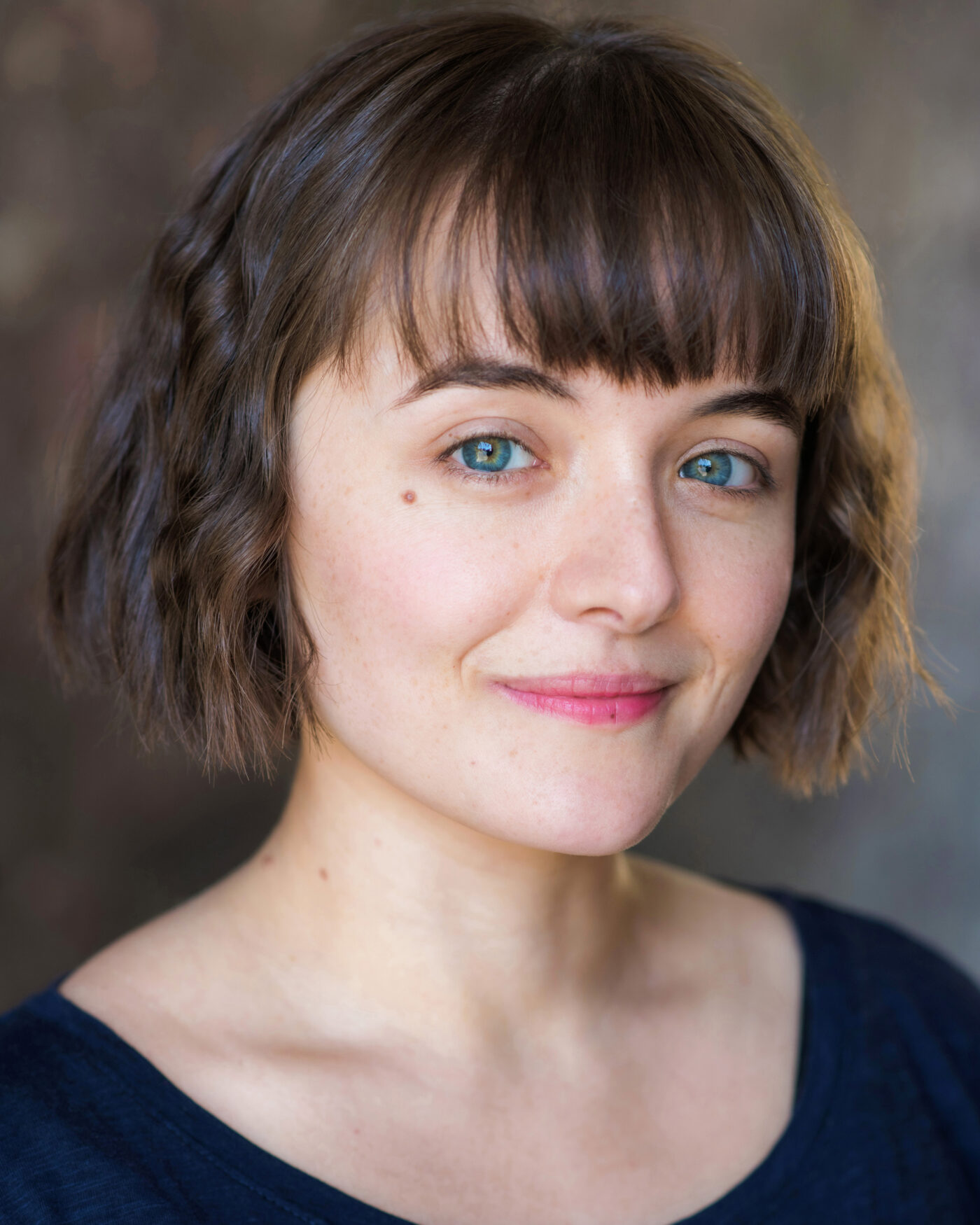 Portrait close-up headshot of Zoe Bullock. A white presenting woman with a brown bob and fringe. She looks directly at the camera.